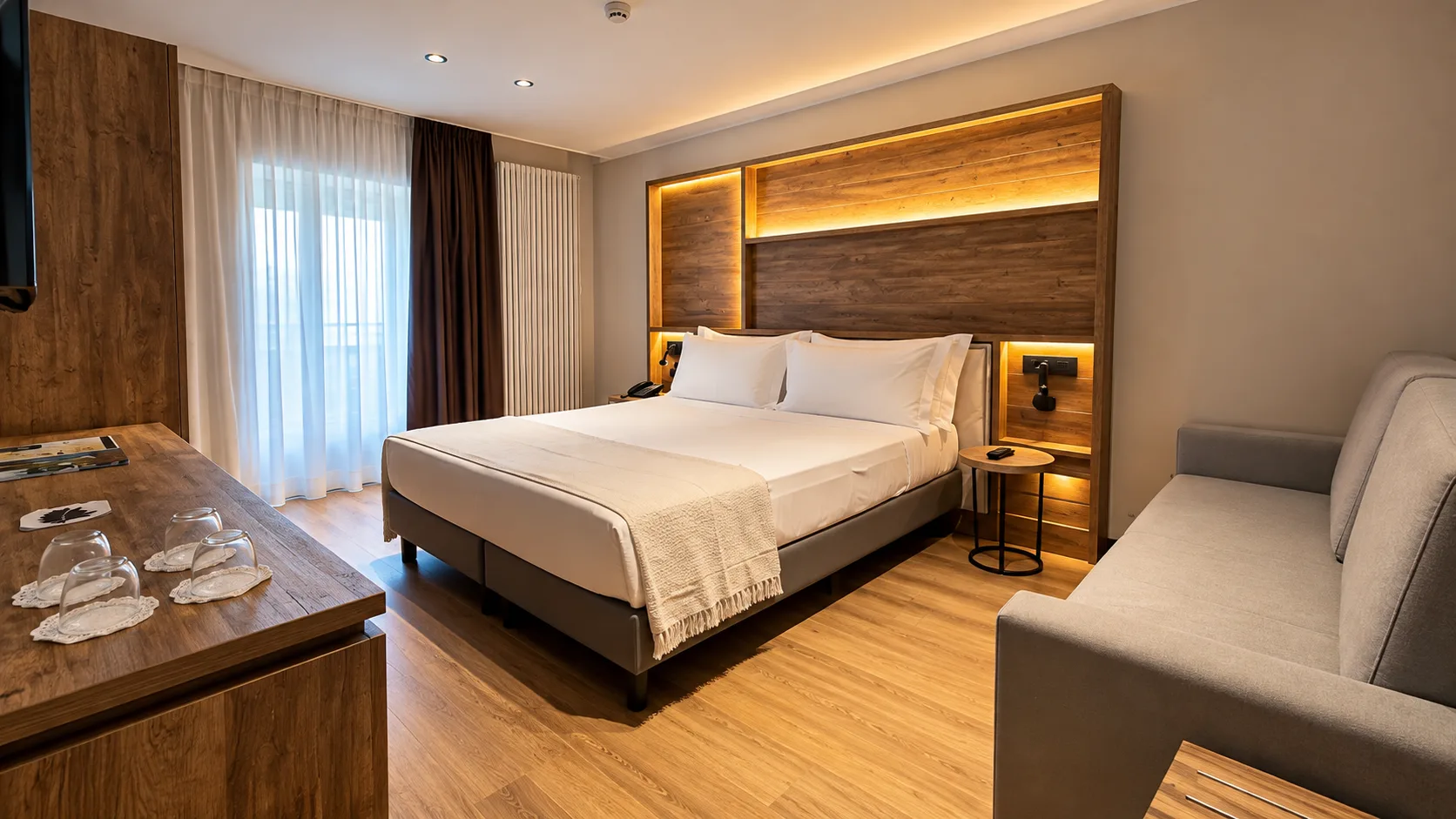 Camera elegante con letto matrimoniale, divano e testiera in legno retroilluminata