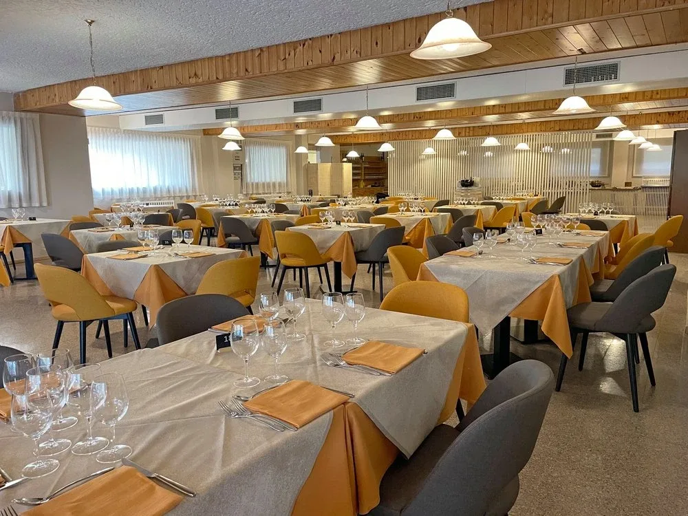 Sala ristorante con tavoli apparecchiati, sedie gialle e grigie e soffitto in legno