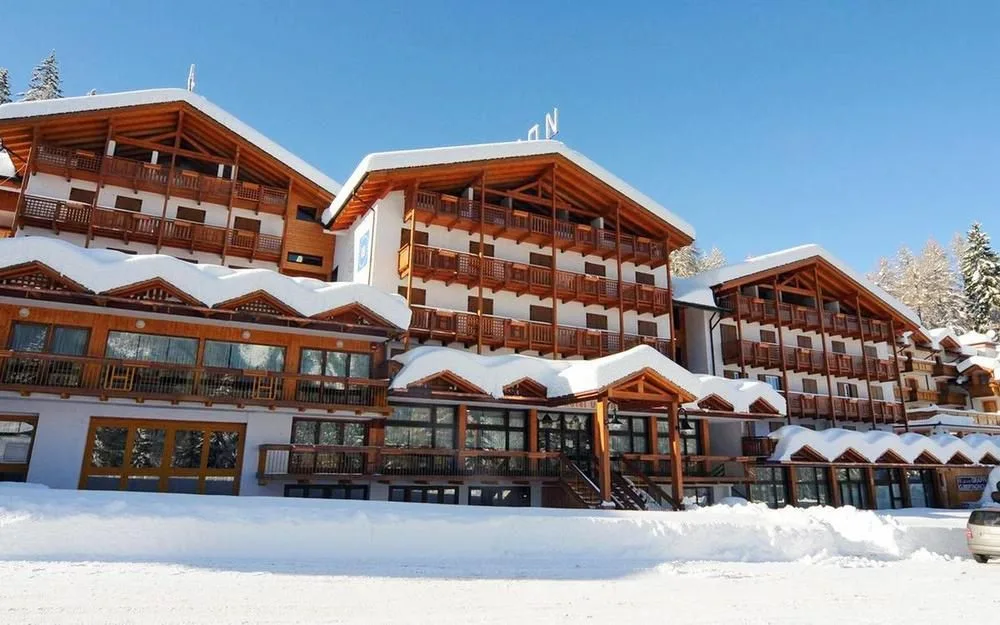 Facciata innevata dell'hotel alpino con ampi balconi in legno e abeti circostanti