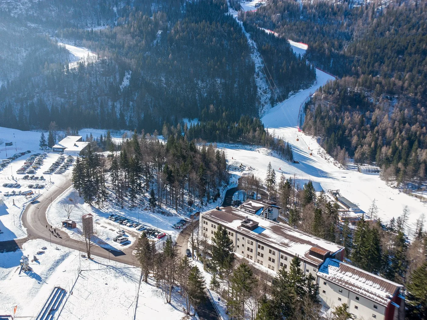 Vista aerea dell'hotel con parcheggio e piste da sci nel bosco innevato