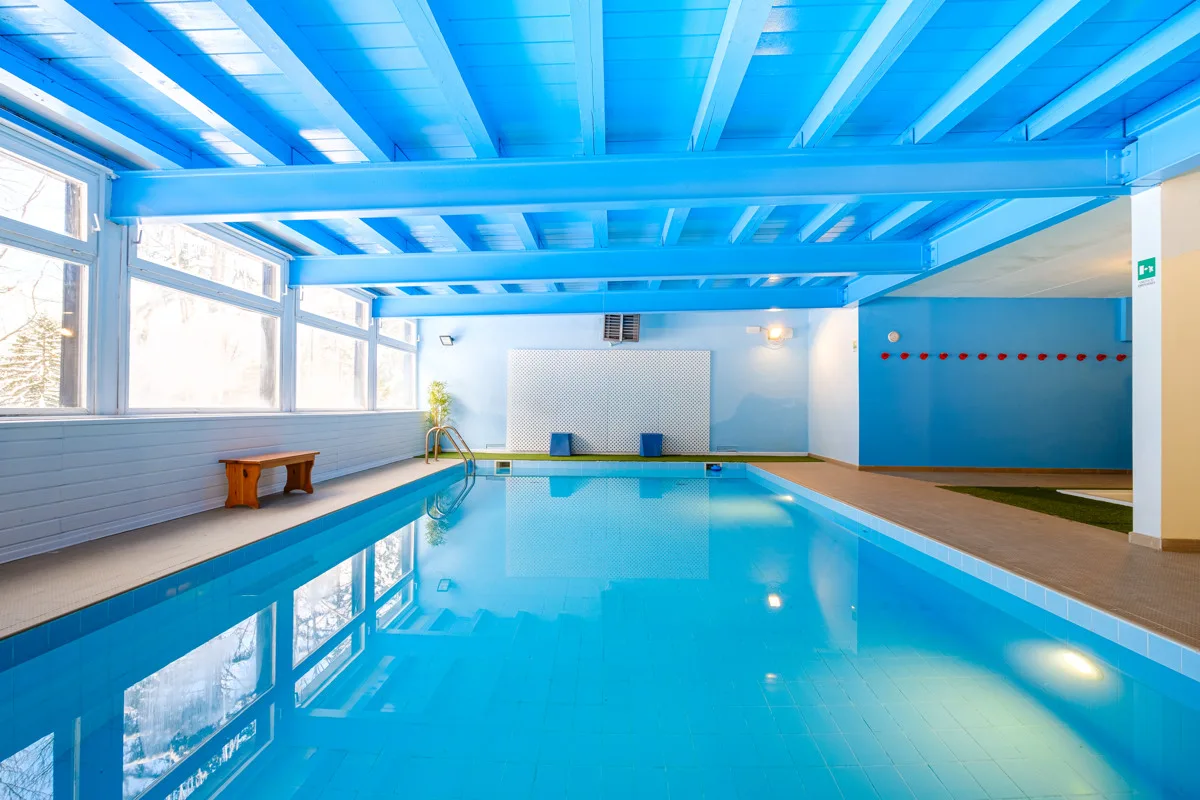 Piscina coperta con soffitto a travi azzurre e ampie vetrate