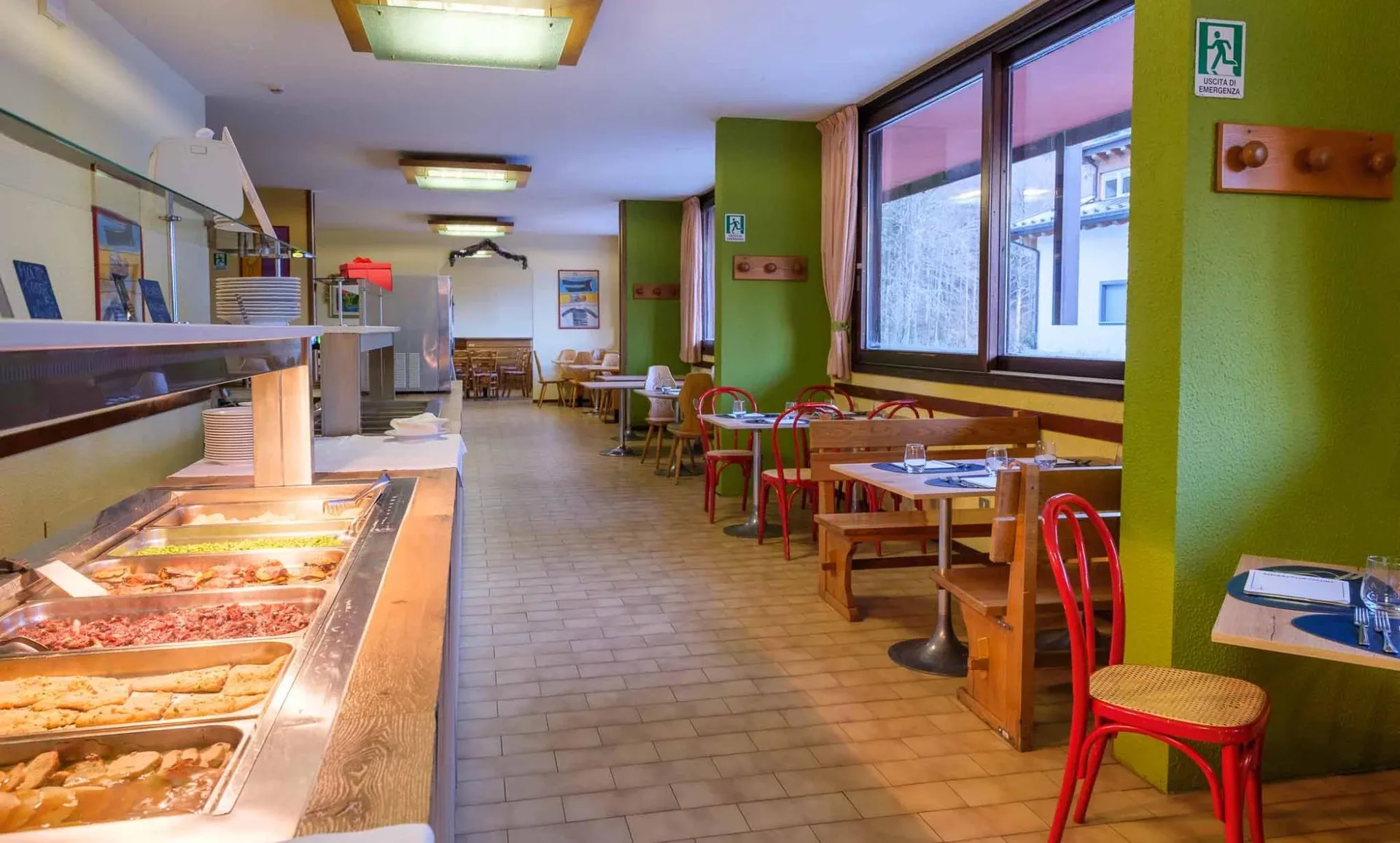 Zona buffet del ristorante con pietanze calde e tavoli in legno