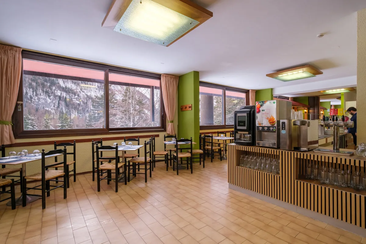 Sala colazioni con tavoli, distributore di bevande e vista sul bosco