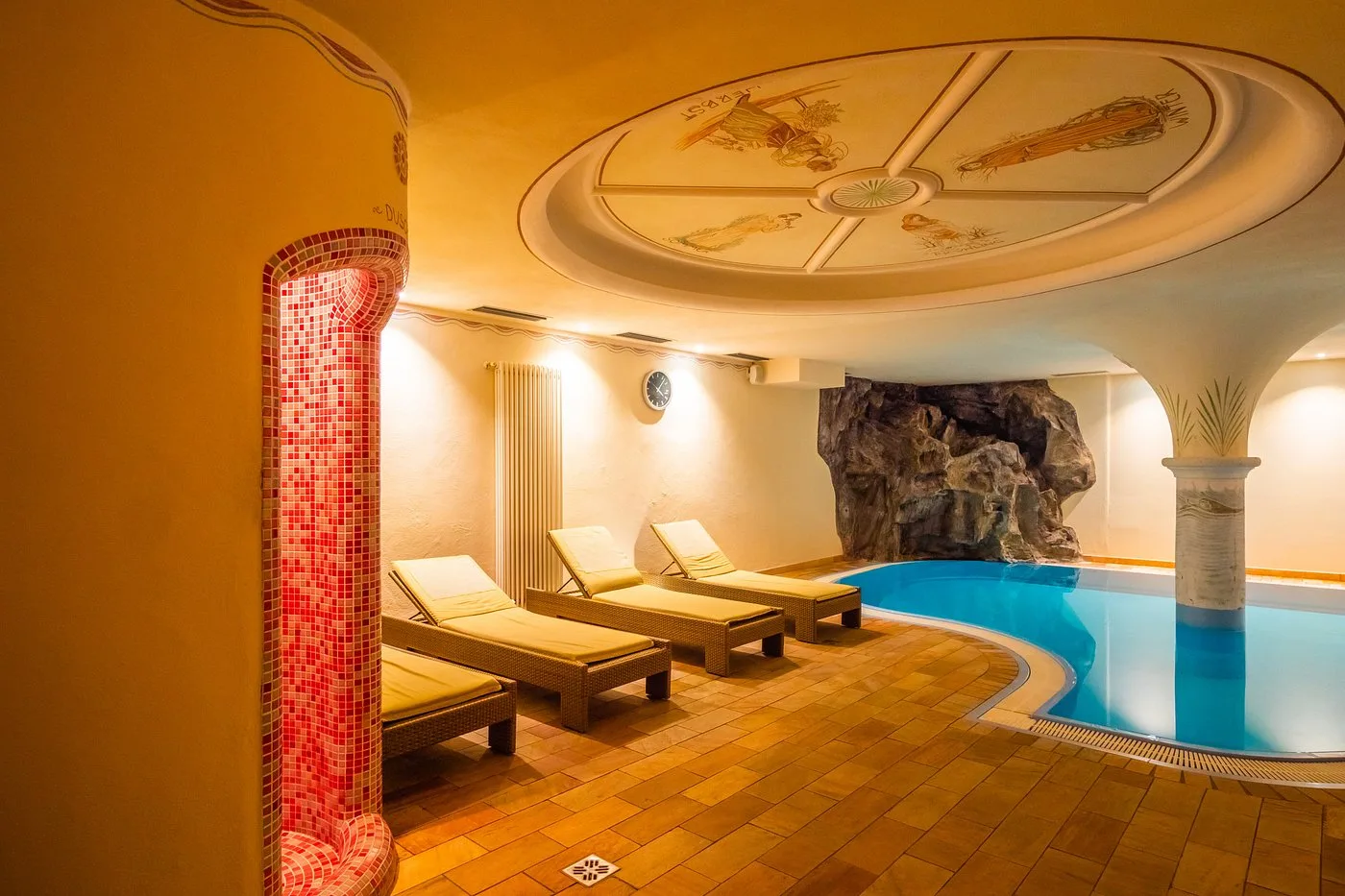 Piscina coperta con grotta artificiale, soffitto decorato e lettini relax