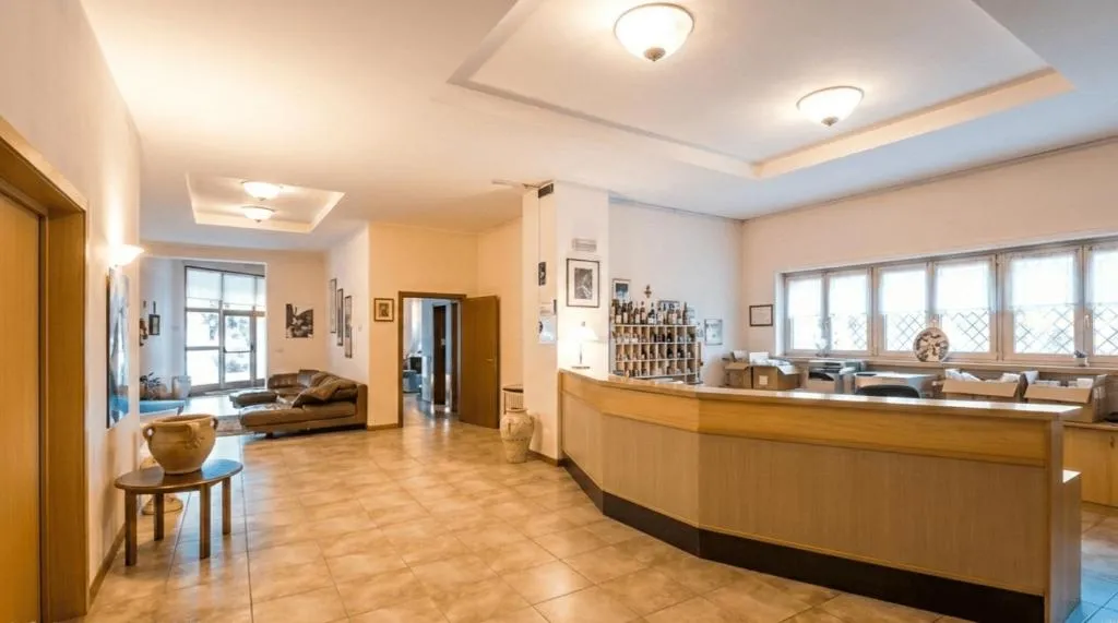 Reception dell'hotel con bancone in legno, pavimento in piastrelle e zona soggiorno con divani