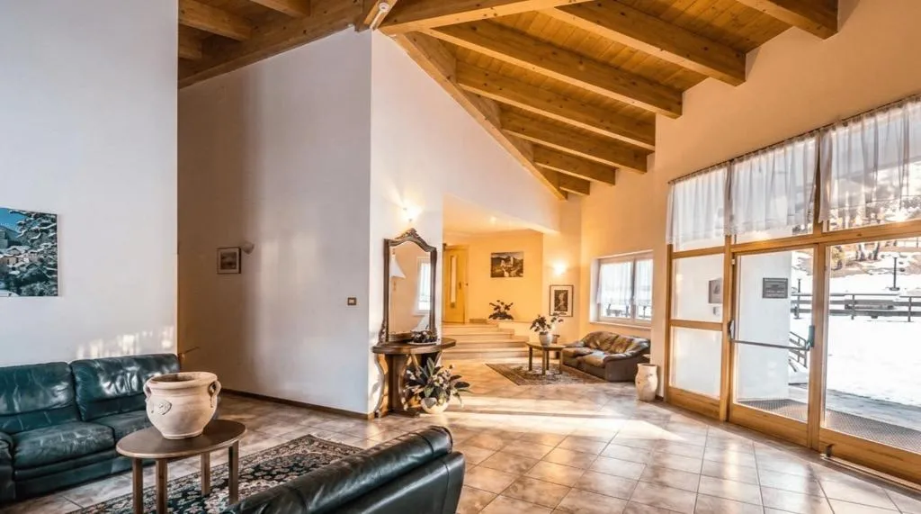 Ampia hall luminosa con soffitto in legno a travi, divani in pelle e grandi vetrate sulla neve