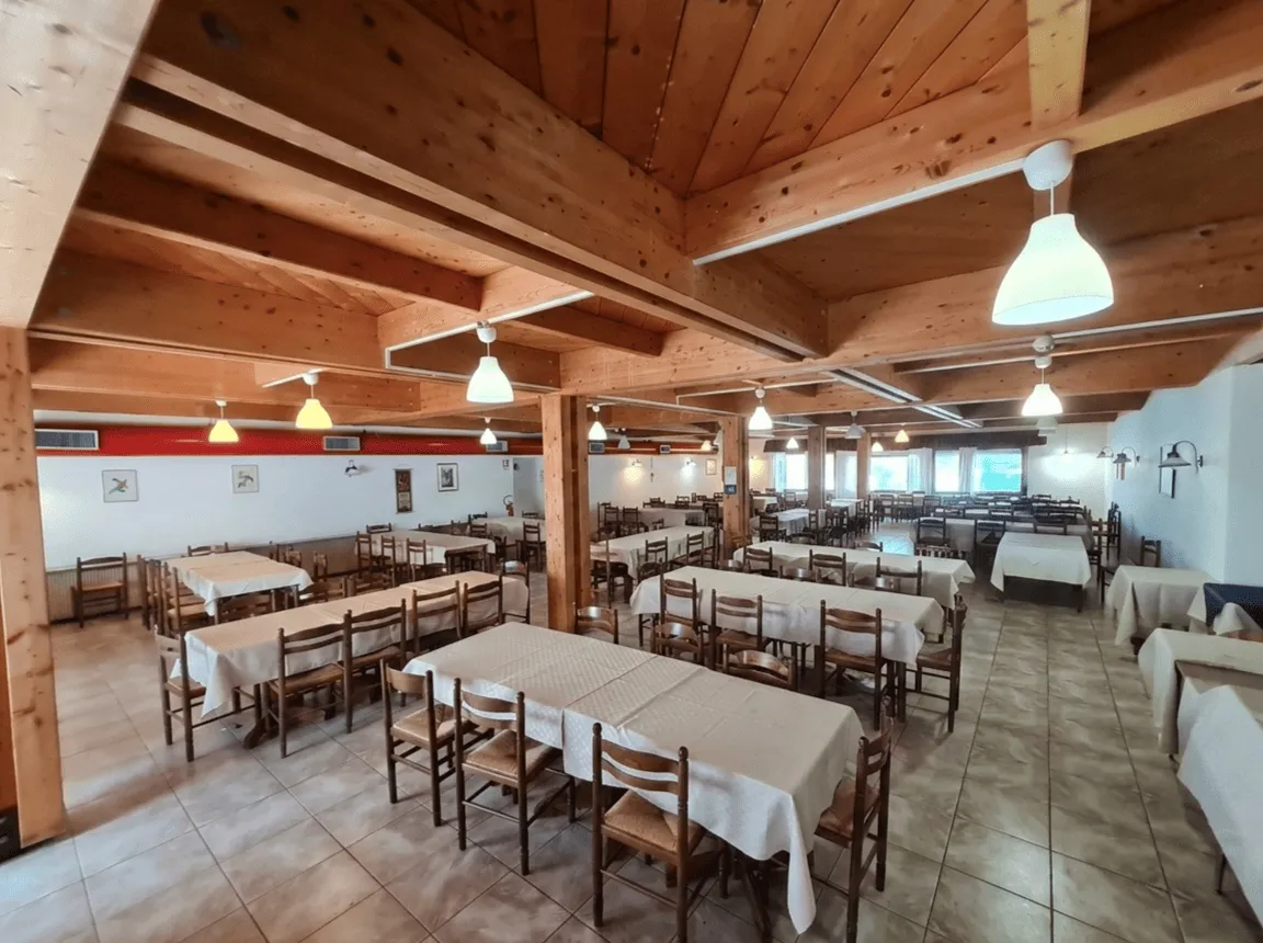 Ampia sala ristorante con soffitto e travi in legno, tavoli apparecchiati con tovaglie chiare