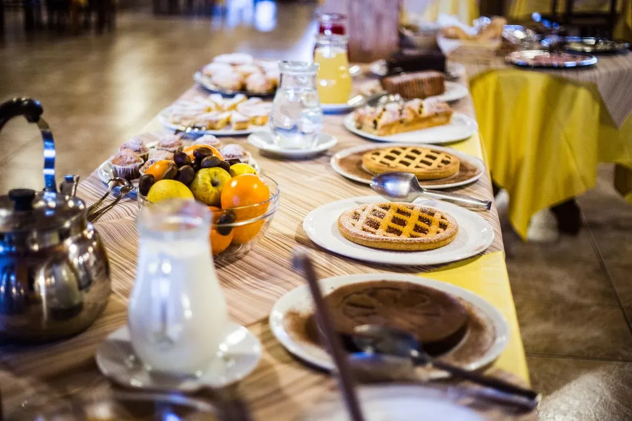 Tavolo del buffet della colazione con crostate, dolci, frutta fresca, latte e succhi
