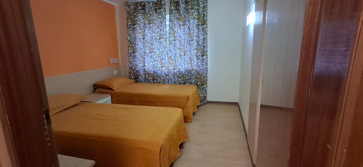 Camera con due letti singoli, copriletti gialli, tenda decorata e armadio a specchio