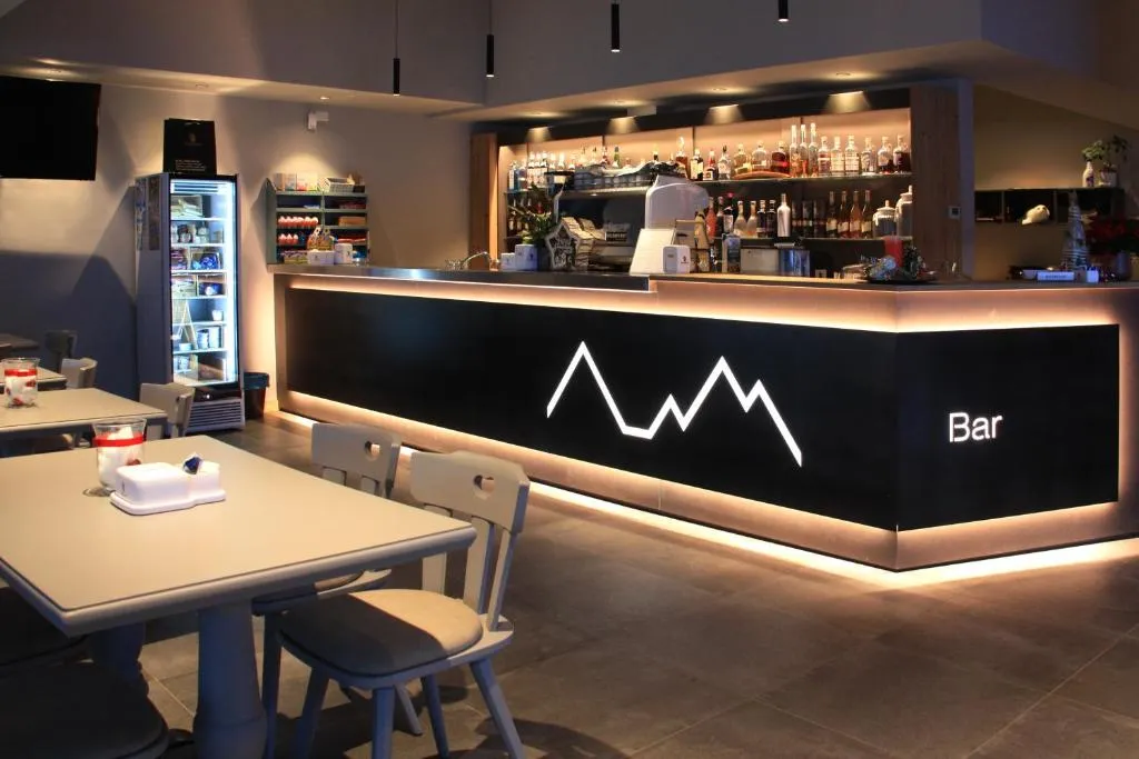 Bancone bar illuminato con logo a forma di montagna e ampia selezione di bottiglie