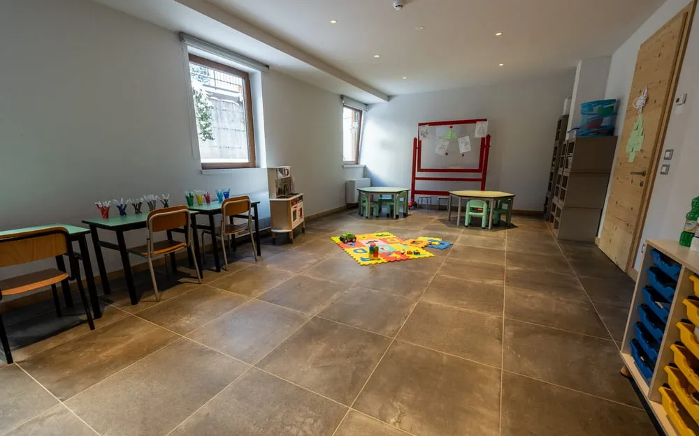 Sala giochi per bambini con tavolini colorati, tappeto e materiale didattico
