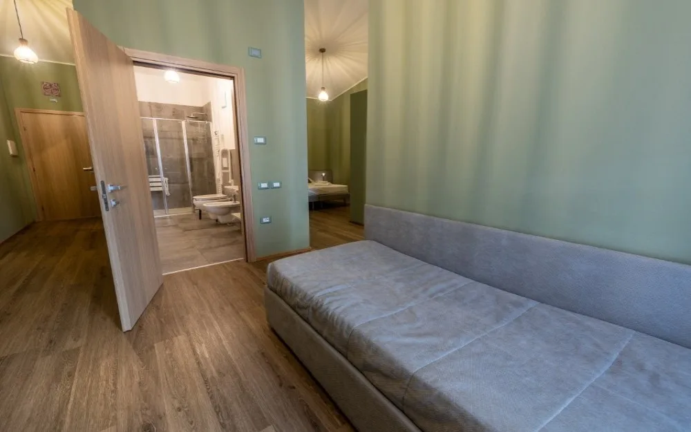 Camera con divano letto grigio, pareti verdi e bagno privato attiguo