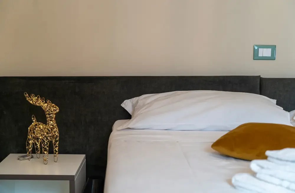 Dettaglio di letto matrimoniale con testiera grigia, decorazione luminosa e cuscino senape