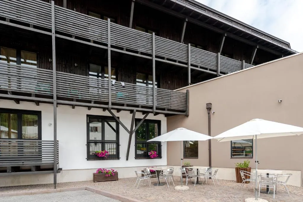 Cortile esterno dell'hotel con tavolini, ombrelloni bianchi e facciata in legno scuro