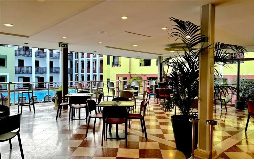 Sala interna con tavoli, sedie, piante e vista sulla piscina