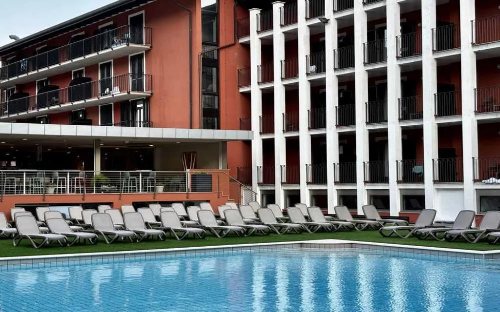 Piscina dell'hotel con lettini allineati e facciata dell'edificio arancione